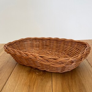 Op de afbeelding: Een geweven rieten mand met een natuurlijke bruine kleur. De mand is ovaalvormig en heeft een gladde, licht afgeronde bodem.