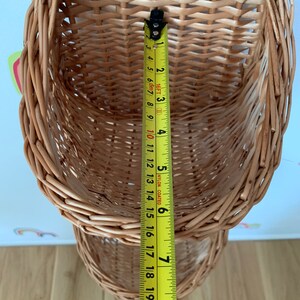 Pu&ograve; includere: Un set di due cesti in vimini intrecciato di colore marrone naturale. I cesti sono impilati uno sopra l'altro e sono appesi al soffitto. Un metro a nastro &egrave; appeso al cesto inferiore, con una misura di 20 cm visibile.