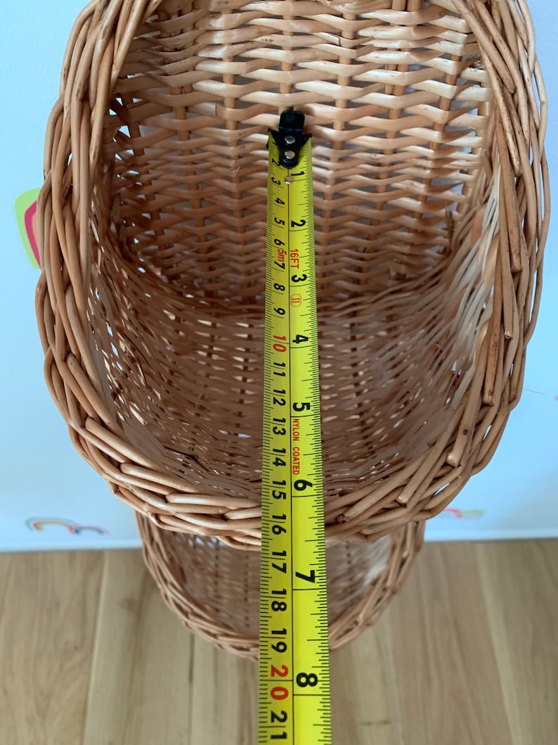 Pu&ograve; includere: Un set di due cesti in vimini intrecciato di colore marrone naturale. I cesti sono impilati uno sopra l'altro e sono appesi al soffitto. Un metro a nastro &egrave; appeso al cesto inferiore, con una misura di 20 cm visibile.