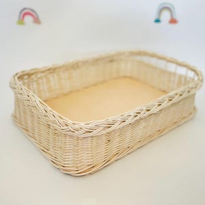 May include: A rectangular woven wicker basket in a light beige colour. The basket is empty and has a smooth, flat base.
