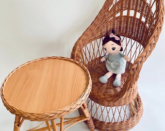 Pode incluir: Uma cadeira de vime com uma boneca sentada nela e uma pequena mesa redonda de vime com tampo de madeira.