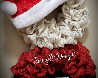 May include: A red and white burlap wreath with a Santa hat on top. The wreath is decorated with a black belt and a silver buckle. The text "TommyBSSDesigns" is visible on the wreath.