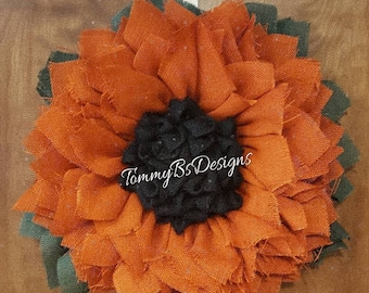 May include: A large orange and green fabric flower wreath with a black fabric center. The wreath has the text "TammyB's Designs" in the center.