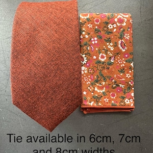 May include: An orange herringbone tie and a matching floral pocket square. The tie is a solid color, while the pocket square features a pattern of small flowers in shades of pink, white, and green on a brown background.