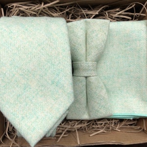 May include: A set of light green accessories for men, including a tie, bow tie, and pocket square. The accessories are made of a soft, textured fabric.