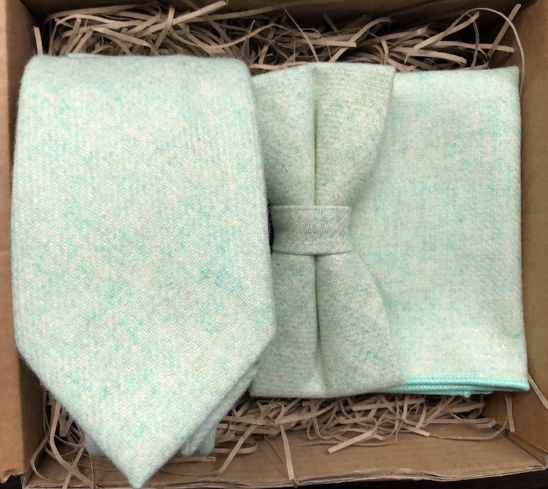 May include: A set of light green accessories for men, including a tie, bow tie, and pocket square. The accessories are made of a soft, textured fabric.