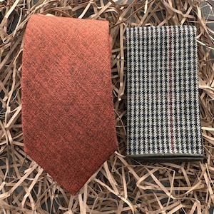 May include: A brown and orange patterned tie and a brown and white patterned pocket square. The pocket square has a red stripe running down the centre.