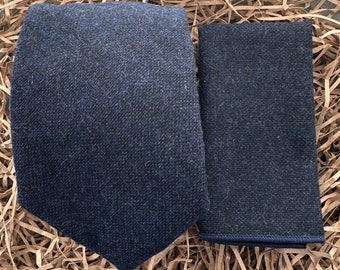 Può includere: Un set di cravatta e fazzoletto da taschino in tinta unita blu scuro e nero sfumato. La cravatta è un degradé dal blu scuro al nero, mentre il fazzoletto da taschino è di un blu scuro pieno.