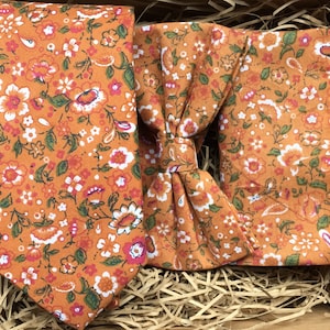 May include: A set of orange and white floral patterned bow tie and necktie. The bow tie and necktie are displayed on a brown paper background.