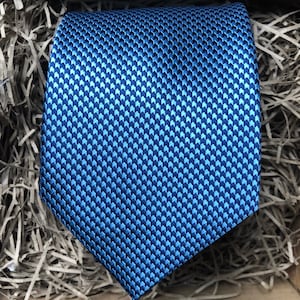 Peut inclure: Une cravate en soie bleue à motif géométrique. La cravate est faite d'un tissu lisse et luxueux.
