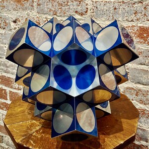 May include: A geometric sculpture made of mirrored glass cubes with blue and silver circles. The sculpture is arranged in a starburst pattern.