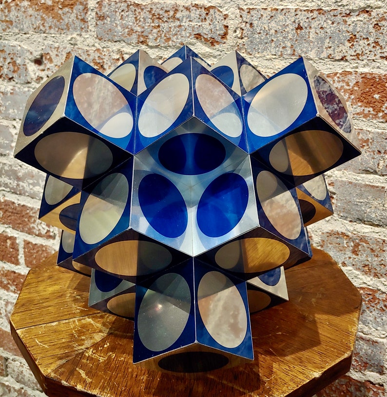 May include: A geometric sculpture made of mirrored glass cubes with blue and silver circles. The sculpture is arranged in a starburst pattern.