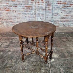 Op de afbeelding: Een ronde houten tafel met ingewikkelde houtsnijwerk op de bovenkant en de poten. De tafel heeft een donkerbruine afwerking en een uniek, open ontwerp.
