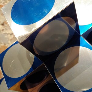 May include: A silver and blue geometric sculpture made of stacked cubes with circular cutouts. Each cube has a blue circle on one side and a silver circle on the other.