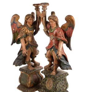 May include: Two carved wooden angels with wings, holding a golden candlestick. The angels are standing on green and gold bases.