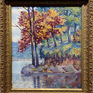 Puede incluir: Una pintura que representa una escena de lago con árboles en primer plano. Los árboles tienen hojas amarillas, naranjas y rojas. El lago es azul y refleja el cielo. La pintura está enmarcada en un marco dorado.