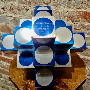 May include: A blue and silver abstract sculpture by artist Vasarely. The sculpture is made of stacked cubes with circles on each face. The text on the sculpture reads "Vasarely - "kros bleu" 1968 editions denise rene paris 1970 n&deg; 105".