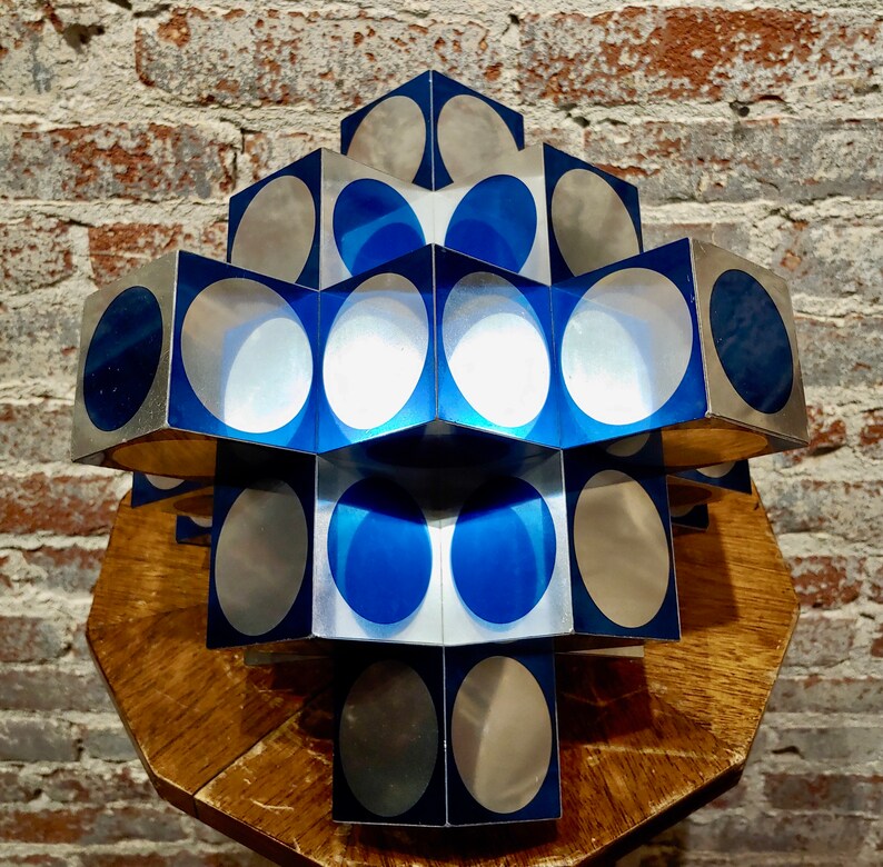 May include: A geometric sculpture made of silver and blue cubes with circular cutouts. The sculpture is arranged in a pyramid shape and is sitting on a wooden surface.