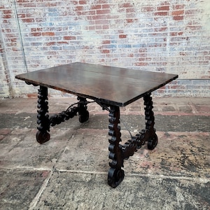 May include: A dark brown wooden table with intricate carved legs. The table has a rectangular top and the legs are scrolled and have a decorative design.