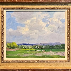 Puede incluir: Pintura al óleo de un paisaje pastoral con un campo verde brillante, árboles y un cielo nublado. La pintura está en un marco dorado y ornamentado. Las vacas pastan en el campo. La firma del artista está en la esquina inferior derecha.