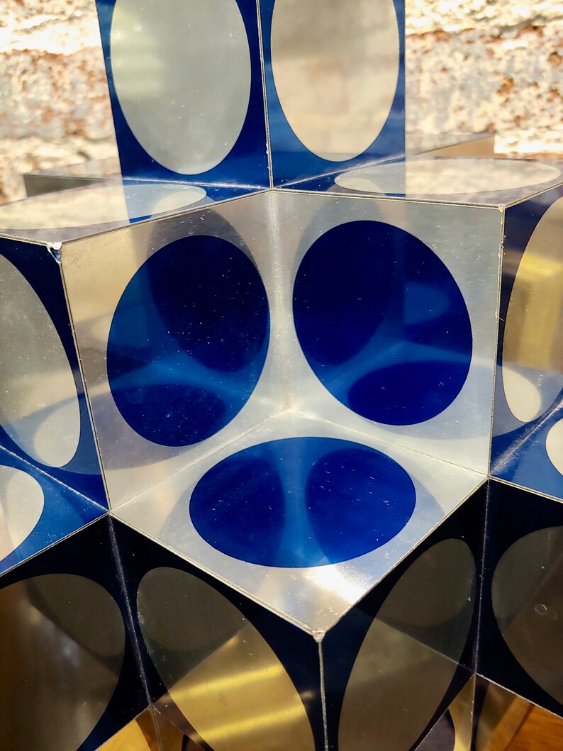 May include: A cube-shaped sculpture made of clear acrylic with blue and silver circles on each side.