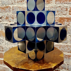 May include: A geometric sculpture made of stacked cubes with alternating silver and blue circular patterns.
