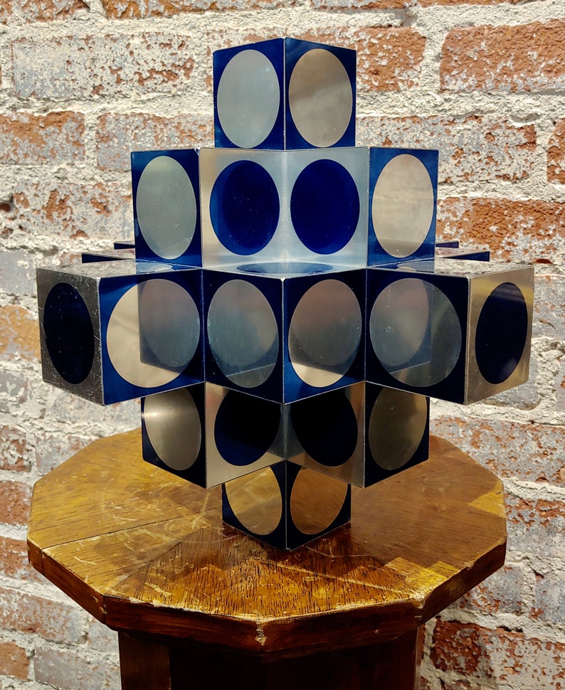 May include: A geometric sculpture made of stacked cubes with alternating silver and blue circular patterns.