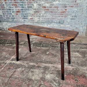 May include: A rustic wooden table with a natural wood finish and four legs. The table has a rough-hewn top and is made of reclaimed wood.