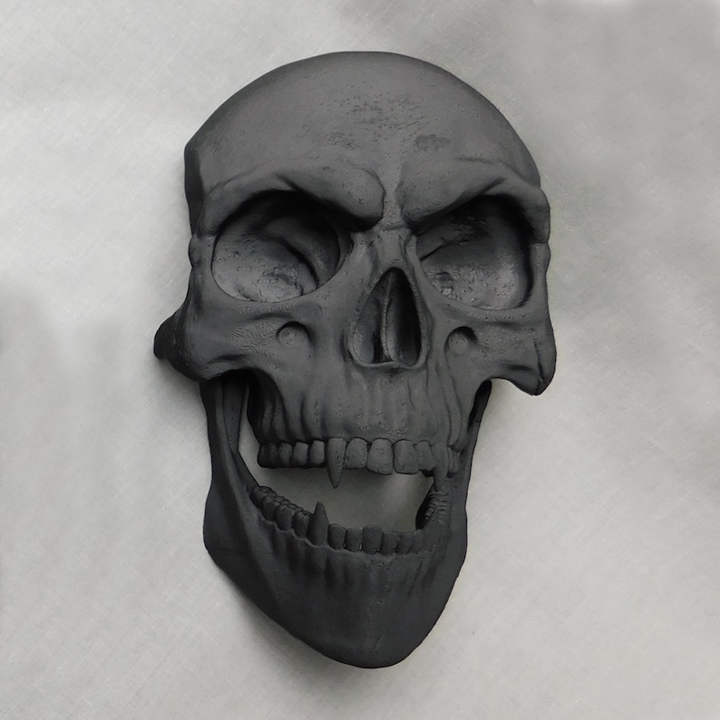 May include: A black skull sculpture with a wide open mouth and sharp teeth. The skull is made of a smooth, matte material and has a realistic appearance.
