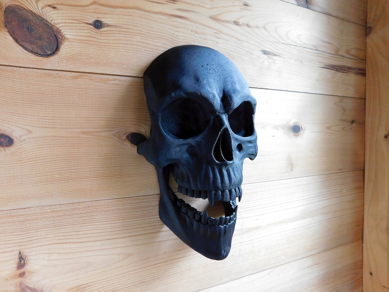 May include: A black skull sculpture with an open mouth and visible teeth, mounted on a wooden wall.