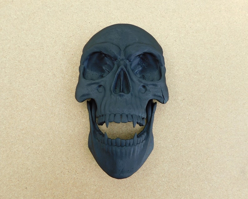 May include: A black skull with a wide open mouth and sharp teeth. The skull is made of a smooth, hard material and has a realistic appearance.