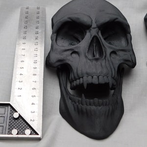 May include: A black skull with a toothy grin, made of a textured material. The skull is approximately 6 inches tall.