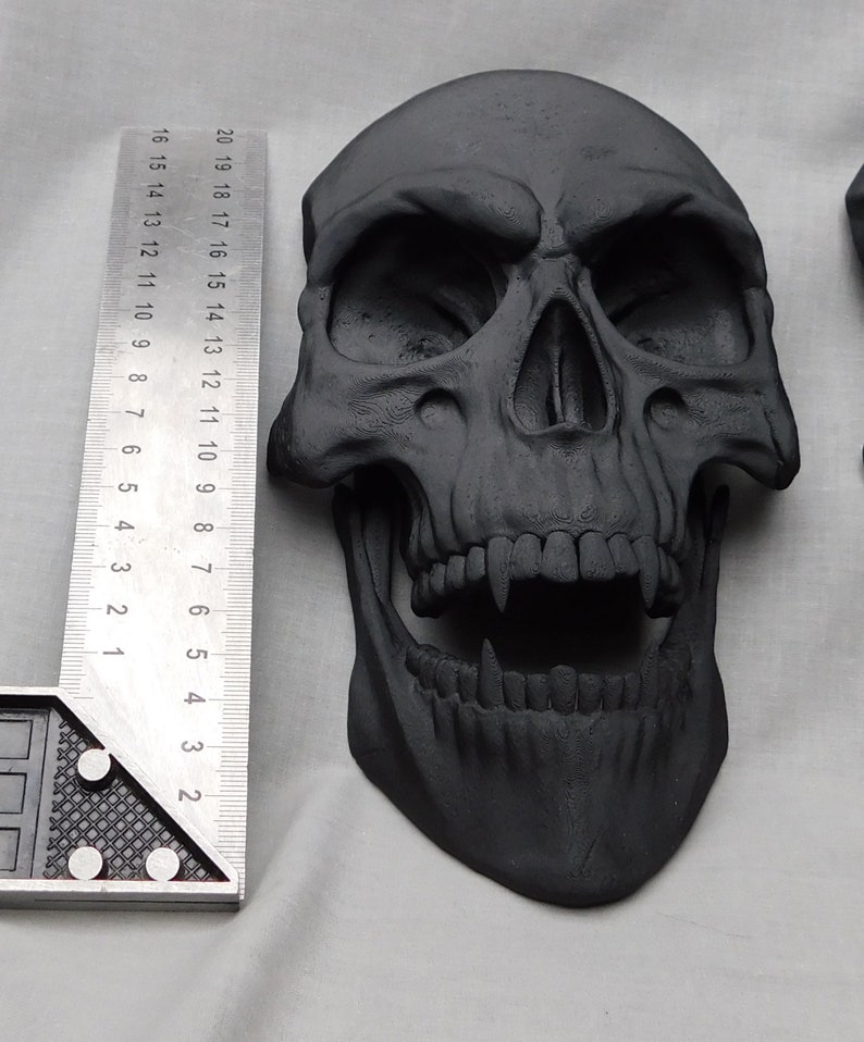 May include: A black skull with a toothy grin, made of a textured material. The skull is approximately 6 inches tall.