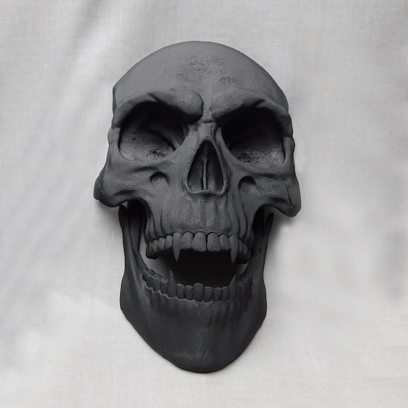 May include: A black skull sculpture with a detailed, open mouth and sharp teeth. The skull is made of a smooth, matte material and has a realistic appearance.
