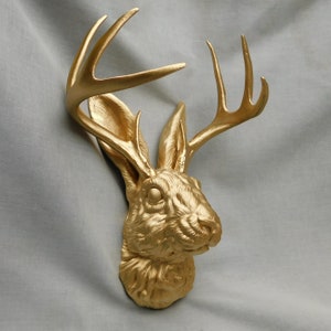 May include: A gold-painted rabbit head with antlers. The rabbit has a realistic, detailed sculpt and is facing to the right. The antlers are long and curved.