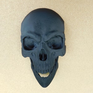 May include: A black skull with an open mouth and visible teeth. The skull is made of a smooth, matte material.