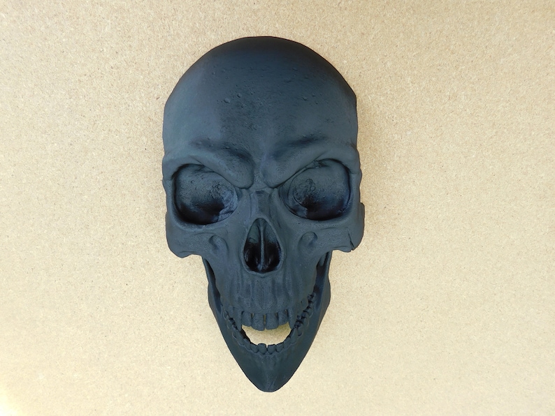 May include: A black skull with an open mouth and visible teeth. The skull is made of a smooth, matte material.