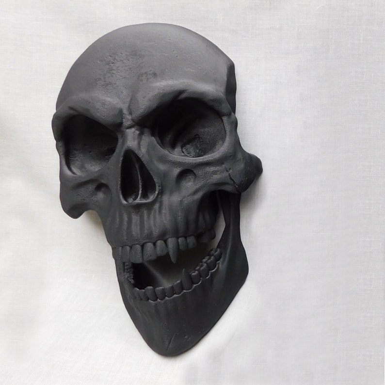 May include: A black skull with a wide open mouth and sharp teeth. The skull is made of a smooth, hard material and has a realistic appearance.