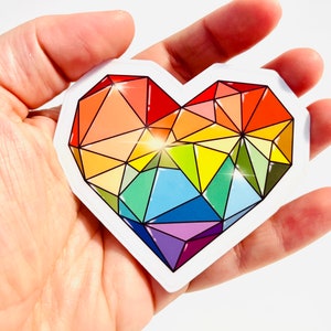 May include: A rainbow heart sticker with a geometric design. The heart is made up of triangles in shades of red, orange, yellow, green, blue, indigo, and violet.