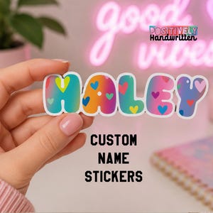 May include: A colorful sticker spelling "HALEY" with a gradient design and heart accents. The sticker is held by a person. The text "CUSTOM NAME STICKERS" is below the name. The background includes a neon sign and a notebook.