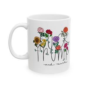 Puede incluir: Taza de café de cerámica blanca con un contorno negro de flores y el texto "F**k Trump and Musk".
