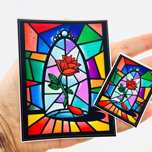 May include: Two stained glass style stickers featuring a single red rose in a glass dome. The larger sticker is approximately 4 inches tall and the smaller sticker is approximately 2 inches tall.