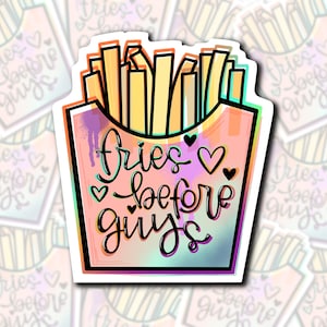 Pode incluir: Um adesivo com fundo arco-íris e borda branca. O adesivo apresenta uma imagem de desenho animado de um recipiente de batatas fritas com batatas fritas dentro. O texto "fries before guys" está escrito em itálico preto com um símbolo de coração.