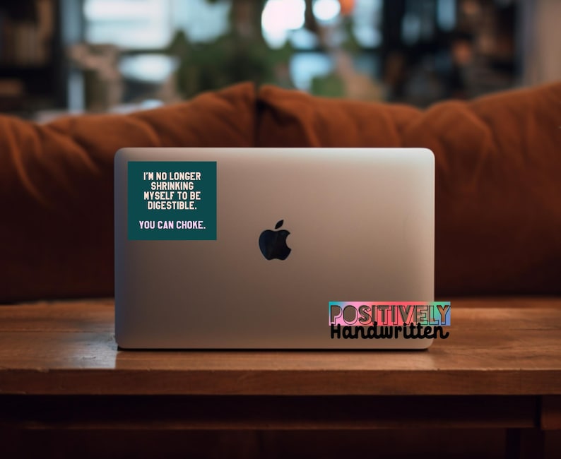 K&ouml;nnte beinhalten: Ein silberner Laptop mit einem schwarzen Apple-Logo. Auf dem Deckel befindet sich ein t&uuml;rkisfarbener Aufkleber mit wei&szlig;em Text, der lautet: "I'M NO LONGER SHRINKING MYSELF TO BE DIGESTIBLE. YOU CAN CHOKE." Darunter befindet sich ein Aufkleber mit der Aufschrift "POSITIVELY Handwritten".