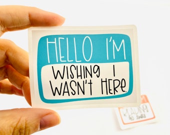 May include: A blue and white sticker with the text "Hello I'm Wishing I Wasn't Here."