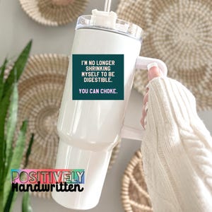 K&ouml;nnte beinhalten: Wei&szlig;er Becher mit Griff und durchsichtigem Deckel. Der Becher hat ein t&uuml;rkisfarbenes Quadrat mit dem Text "I'M NO LONGER SHRINKING MYSELF TO BE DIGESTIBLE. YOU CAN CHOKE." Auf dem Becher steht "POSITIVELY Handwritten."