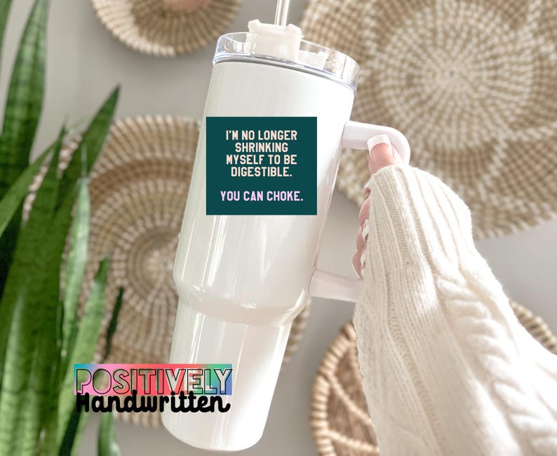 K&ouml;nnte beinhalten: Wei&szlig;er Becher mit Griff und durchsichtigem Deckel. Der Becher hat ein t&uuml;rkisfarbenes Quadrat mit dem Text "I'M NO LONGER SHRINKING MYSELF TO BE DIGESTIBLE. YOU CAN CHOKE." Auf dem Becher steht "POSITIVELY Handwritten."