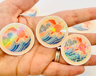 Puede incluir: Tres pegatinas iridiscentes con un diseño retro de sol, olas y nubes. Las pegatinas son redondas y tienen un acabado holográfico.