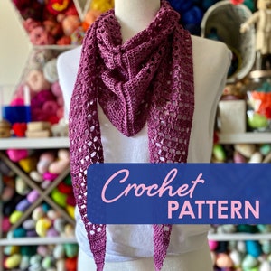 Puede incluir: Un patrón de crochet para una chal de color morado con un diseño de encaje. El chal está drapeado sobre un maniquí blanco. El texto "Crochet Pattern" se muestra sobre un fondo azul.
