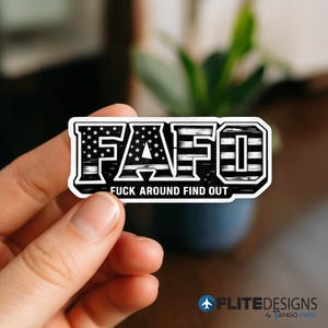 May include: A rectangular sticker with the letters "FAFO" in a bold, blocky font. The "FA" is filled with a stars and stripes design, and the text "FUCK AROUND FIND OUT" is printed below the letters. The sticker has a white border.